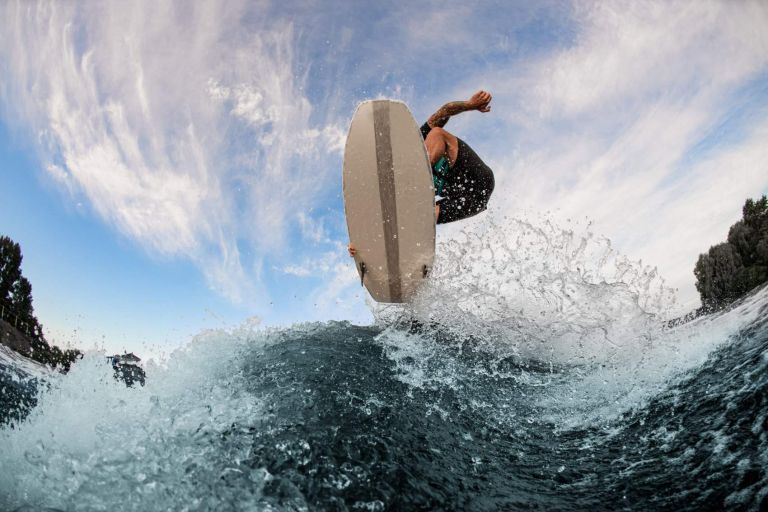 beautiful view of a wakesurf board and a male athlete jumping in the air above a splashing wave